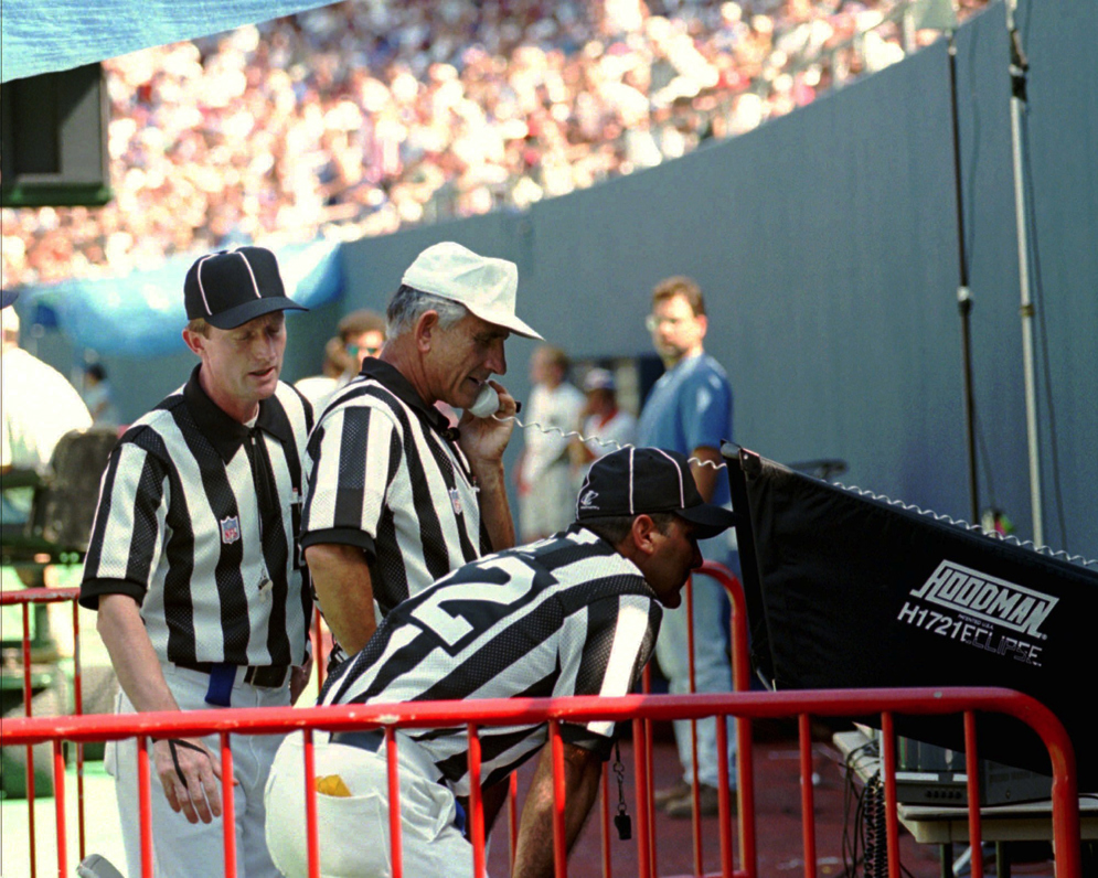 El &#xE1;rbitro principal Bob McElwee revisa una jugada con un monitor en el campo durante la prueba del nuevo sistema en la pretemporada de 1996. (Fotograf&#xED;a de AP/Bill Kostroun)